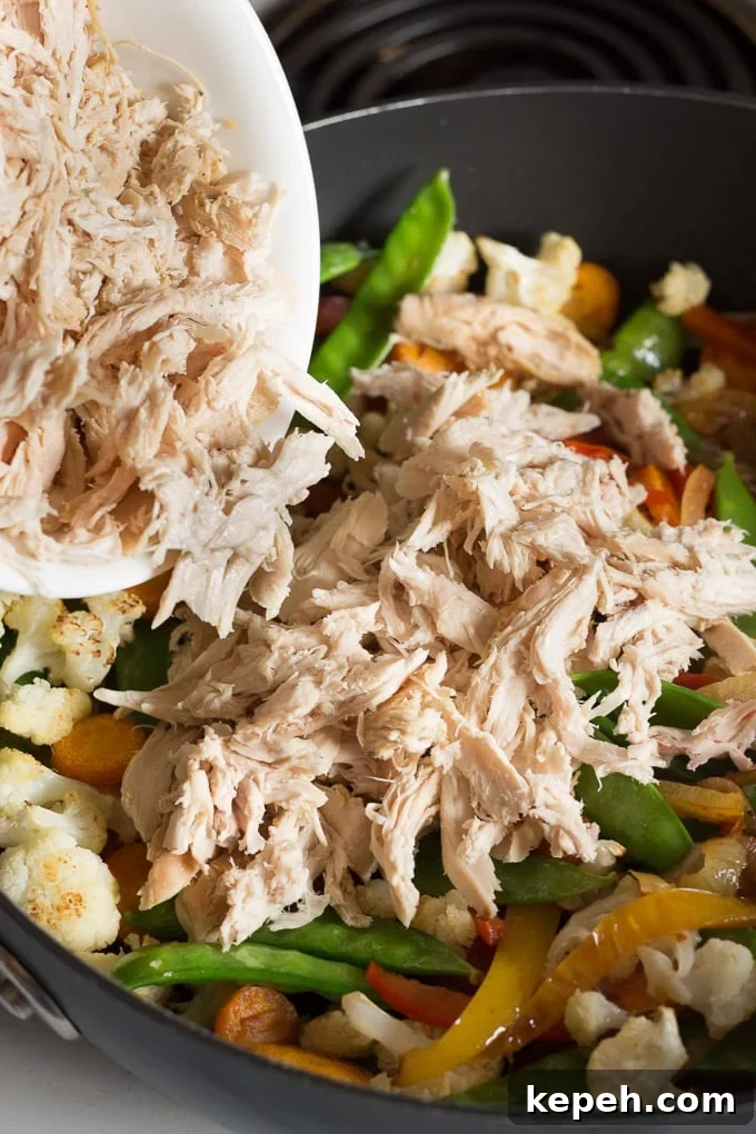 shredded chicken being added to a frying pan with sauteed onions, bell peppers, and snow peas