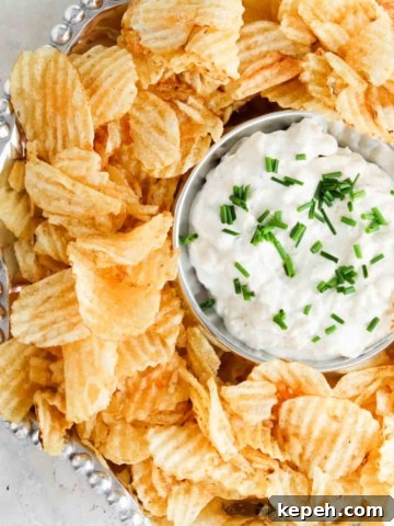 Pretty french onion dip in a silver bowl with potato chips and chives on top.