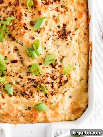 Crab dip in a white casserole dish with green onions and red pepper flakes on top.