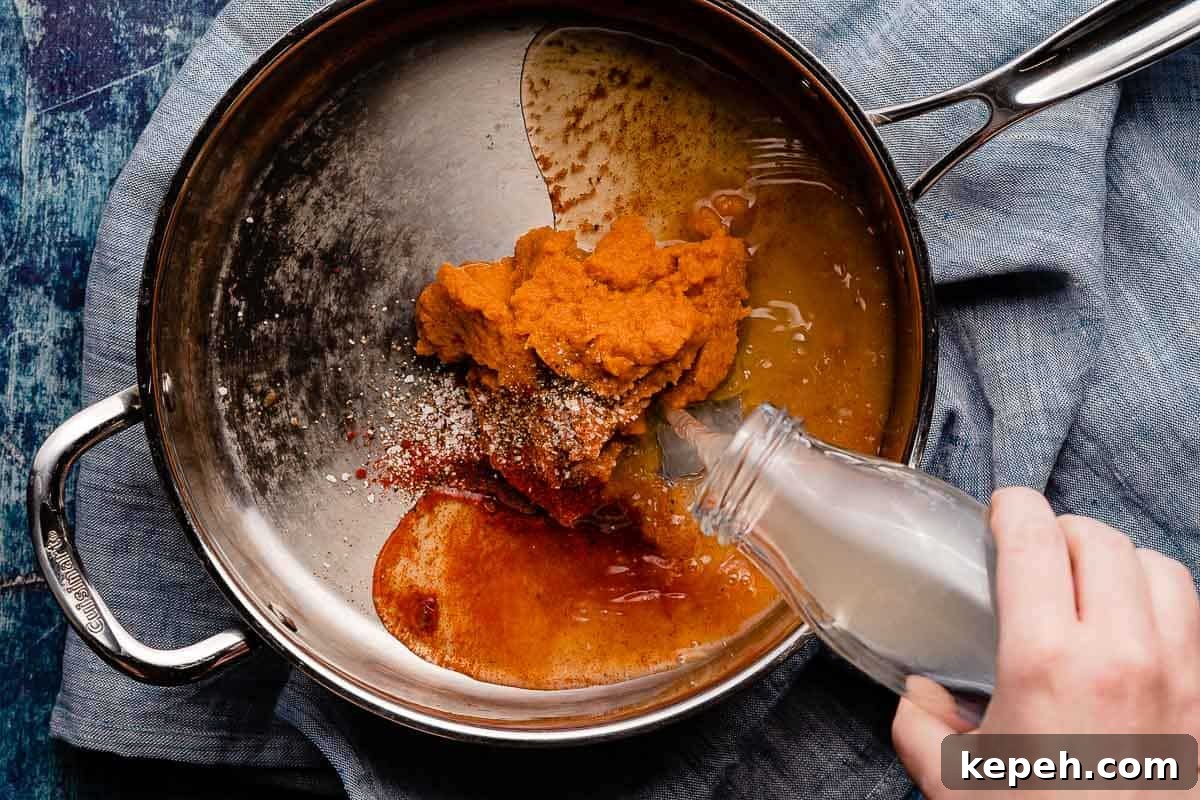 hand pouring broth into pan with pumpkin and spices