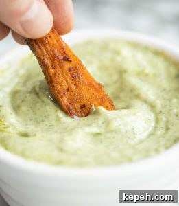 Sweet potato wedges and pesto mayo closeup shot of dunking sweet potato wedge into pot of pesto mayo
