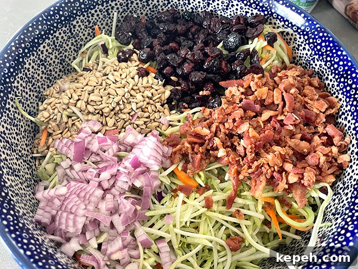 A large white and dark blue bubble patterned Polish pottery serving bowl with broccoli slaw, bacon crumbles, diced red onion, sunflower seeds, and Craisins.