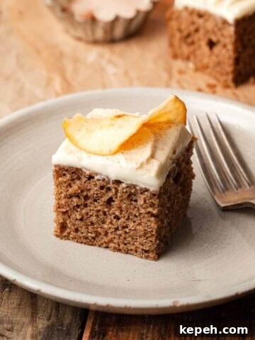a slice of gluten free applesauce cake topped with cream cheese frosting and an apple chip on a plate with a fork