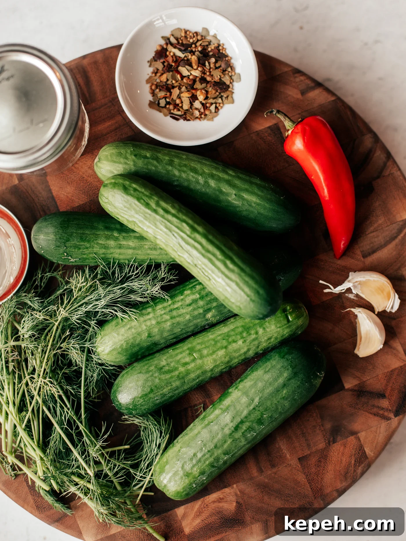 Quick Refrigerator Pickles: Crisp No-Cook Dill Recipe 3 Cutting board with mini cucumbers, fresh dill, red chili, garlic cloves, jars, and pickling spice.