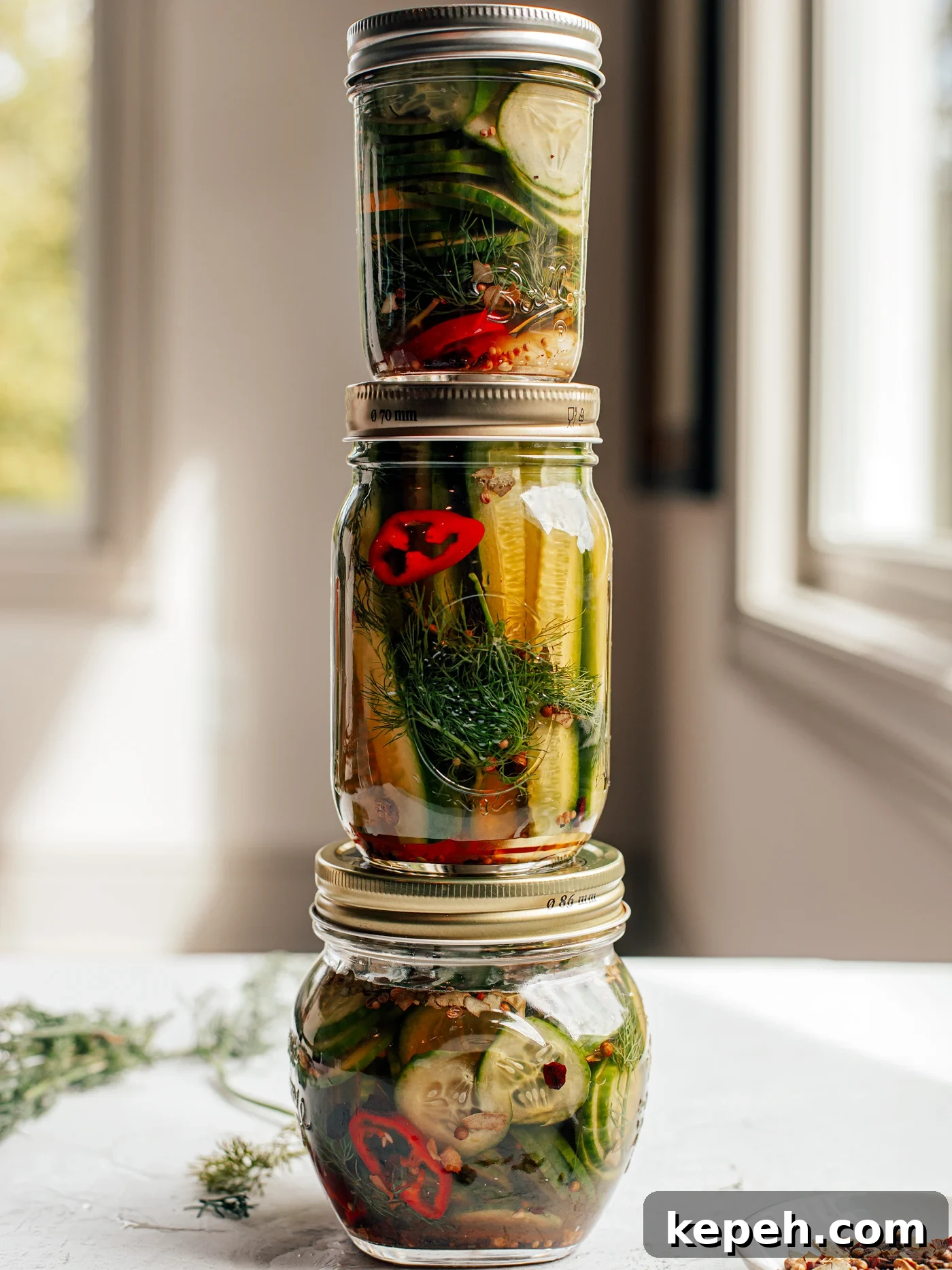 Quick Refrigerator Pickles: Crisp No-Cook Dill Recipe 5 Three different sized jars of refrigerator pickles stacked on top of one another on a countertop.