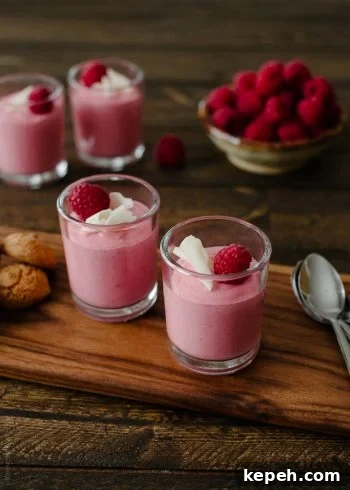 Small glass cups of raspberry mousse garnished with white chocolate and raspberries.