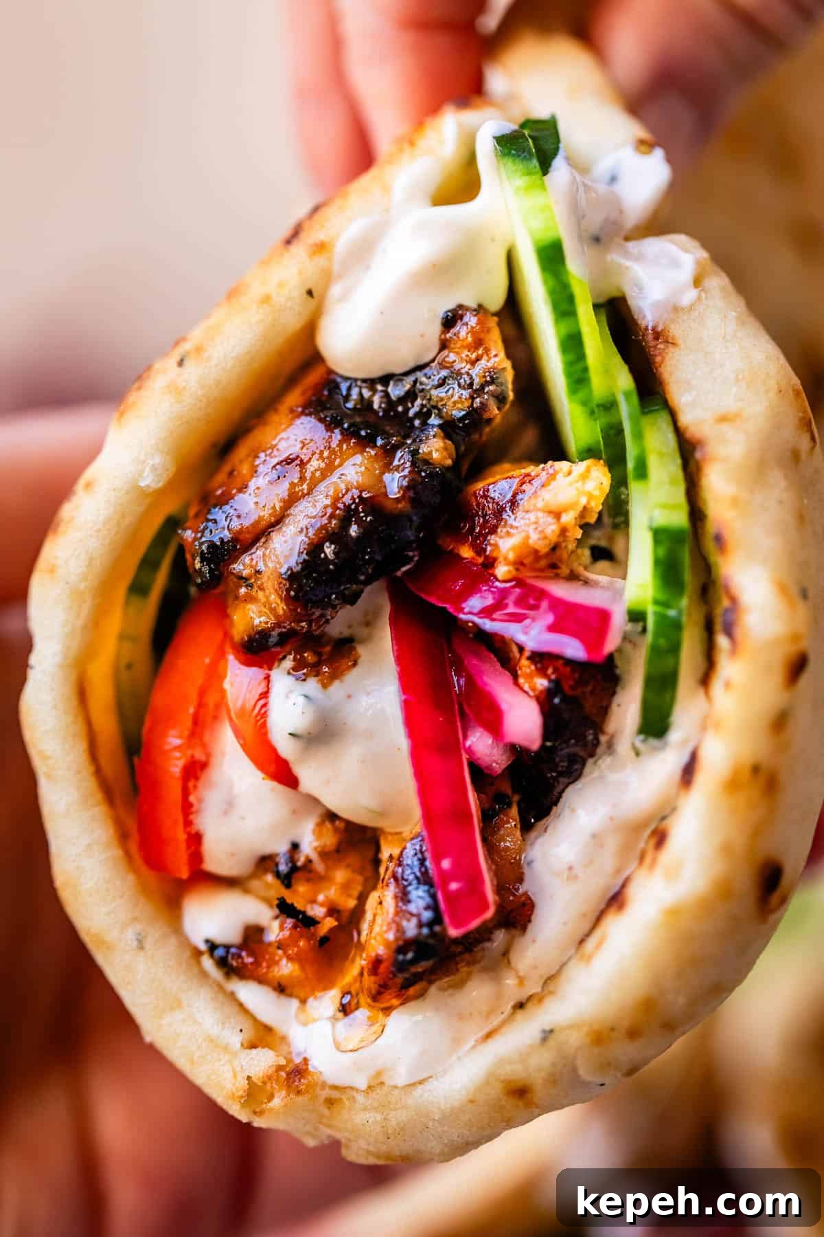Authentic Chicken Shawarma Recipe: Juicy Middle Eastern Wraps 14 hand holding chicken shawarma in naan with cucumber, onion, and garlic sauce.