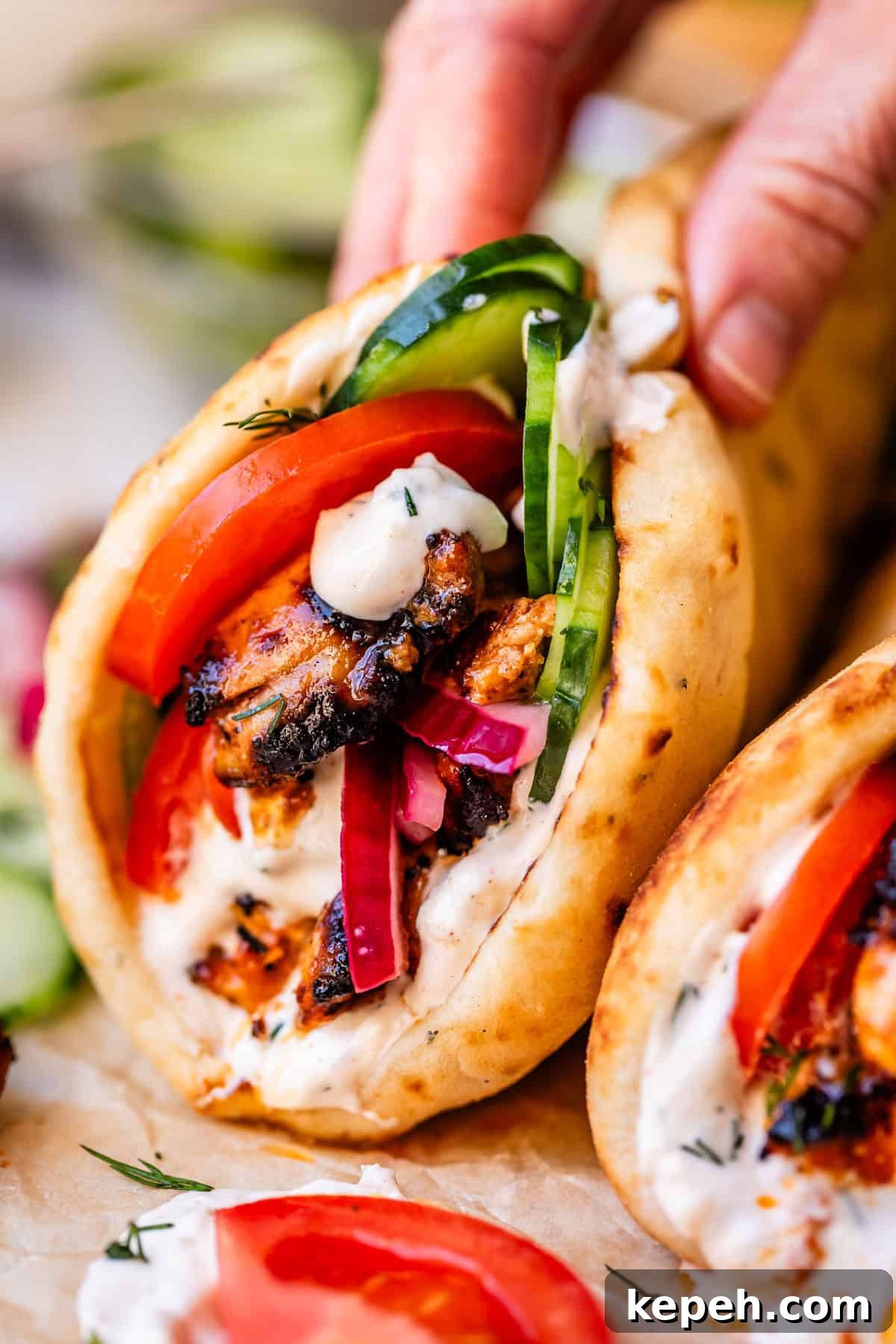 Authentic Chicken Shawarma Recipe: Juicy Middle Eastern Wraps 16 hand holding a chicken shawarma wrap with all the fixings and sitting on parnchment.