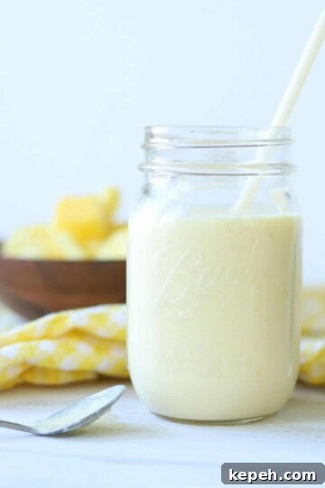 mango pineapple smoothie in a mason jar with a straw with yellow and white checkered napkin and wooden bowl full of mango and pineapple