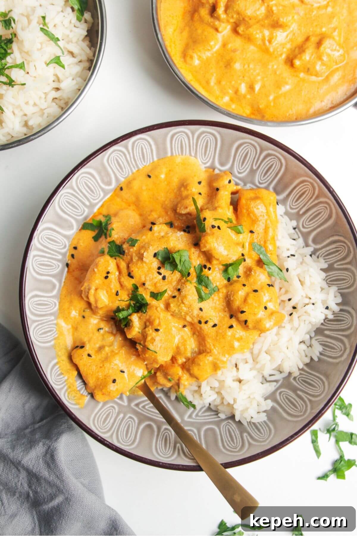 Chicken korma curry on top of rice in a bowl, with more curry and rice on the side.