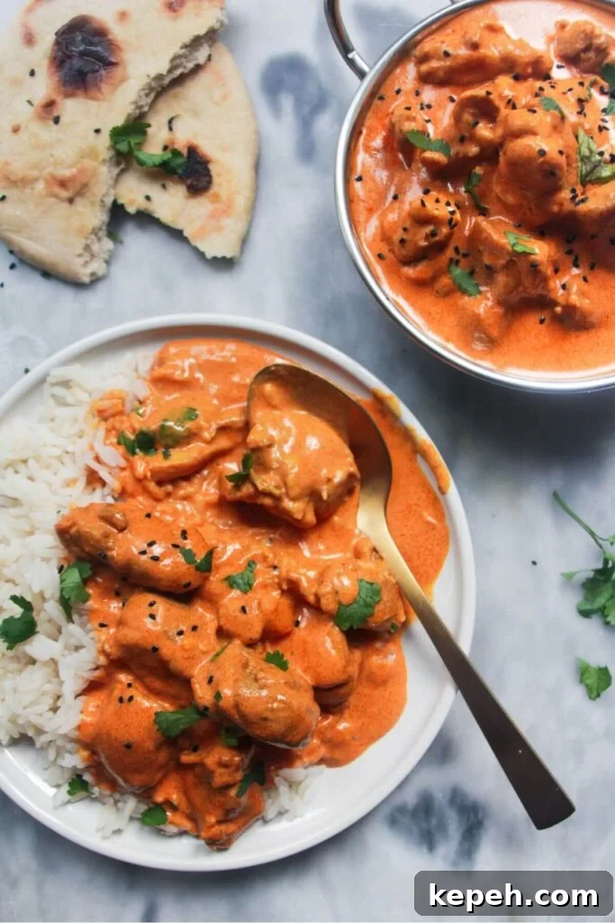 White plate with rice and butter chicken with bowl of butter chicken in the background and garlic naan.