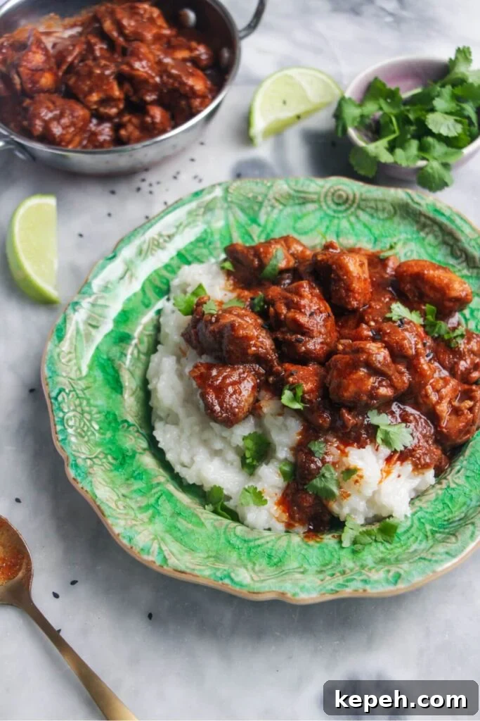 Close up of chicken rogan josh on rice on a small green plate with more curry in the background.