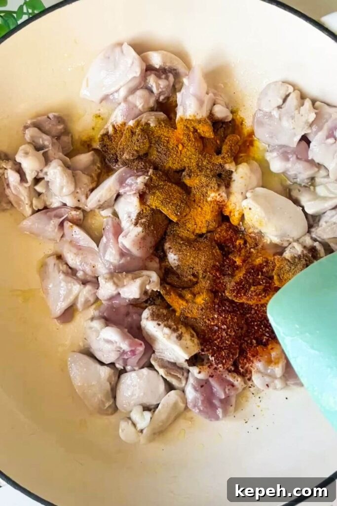 Spices added to cooked chicken pieces in a pan.