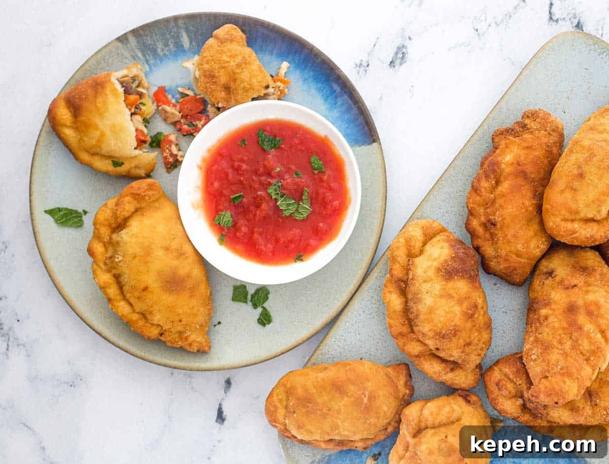 Panzerotti (mini calzone pizza with tuna & red peppers) | www.cookeatworld.com Panzerotti sits on a plate with the filling on show of olives, tuna, egg and red pepper alongside a small dish of tomato sauce