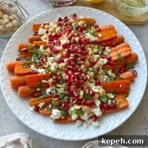 Side view of oven roasted carrots topped with feta, pomegranate, and hasselnuts. A few ingredients are seen in the background.
