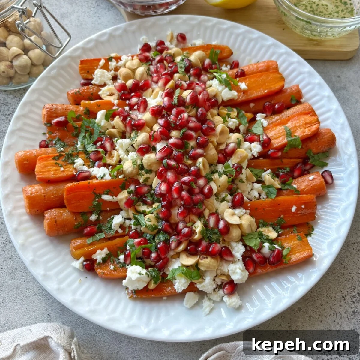 Side view of oven roasted carrots topped with feta, pomegranate, and hasselnuts. A few ingredients are seen in the background.