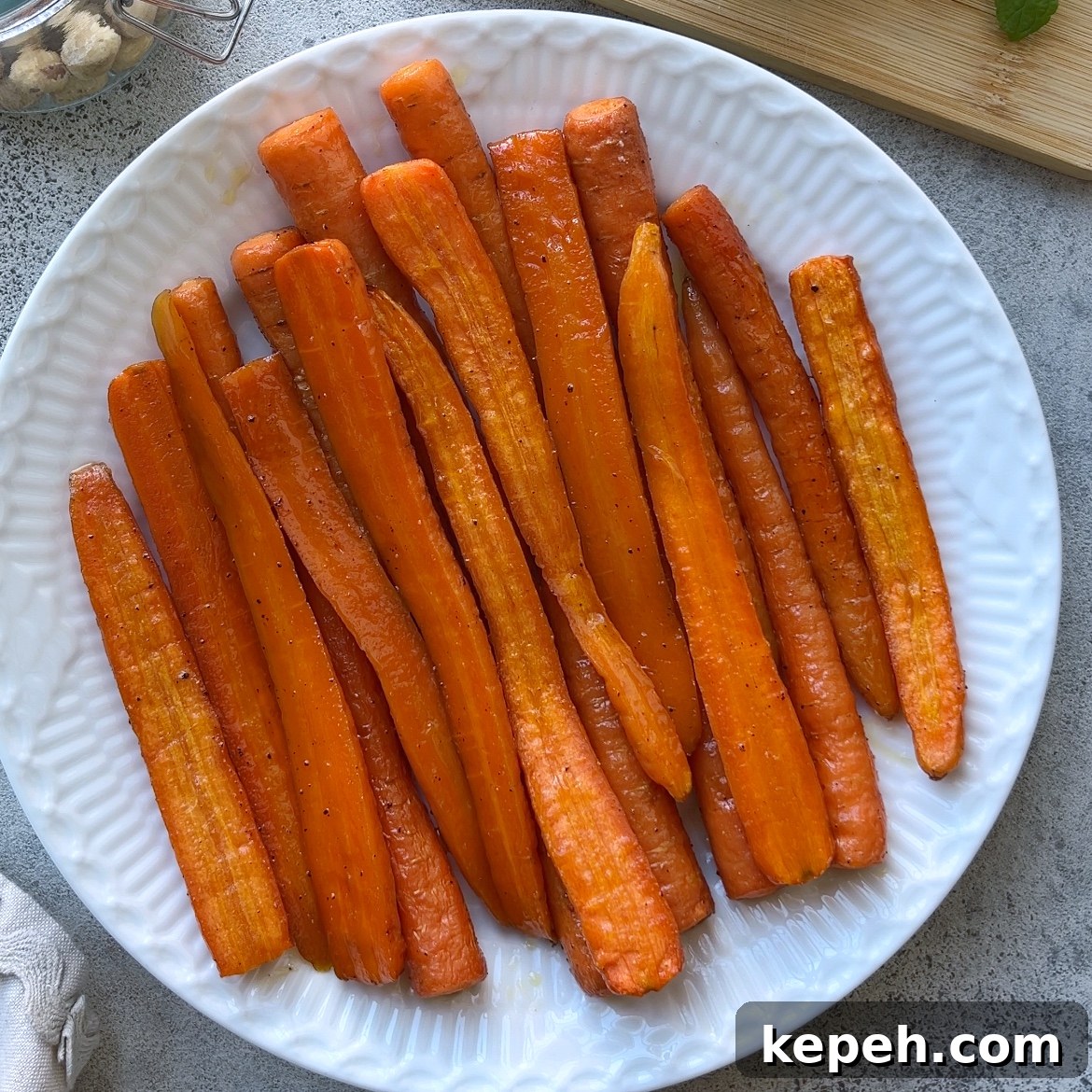 A white plate filled with Roasted Maple Carrots, lightly seasoned and arranged in a single layer on a gray surface.