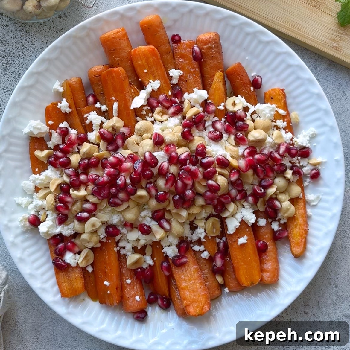 Roasted Maple Carrots on a white plate topped with crumbled feta, pomegranate seeds, and chopped hazelnuts.