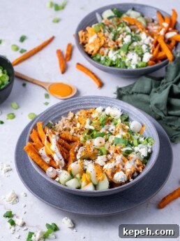 bowl with brown rice, shredded buffalo chicken, green onions, lettuce, cucumber, sweet potato fries, feta, buffalo sauce and ranch dressing