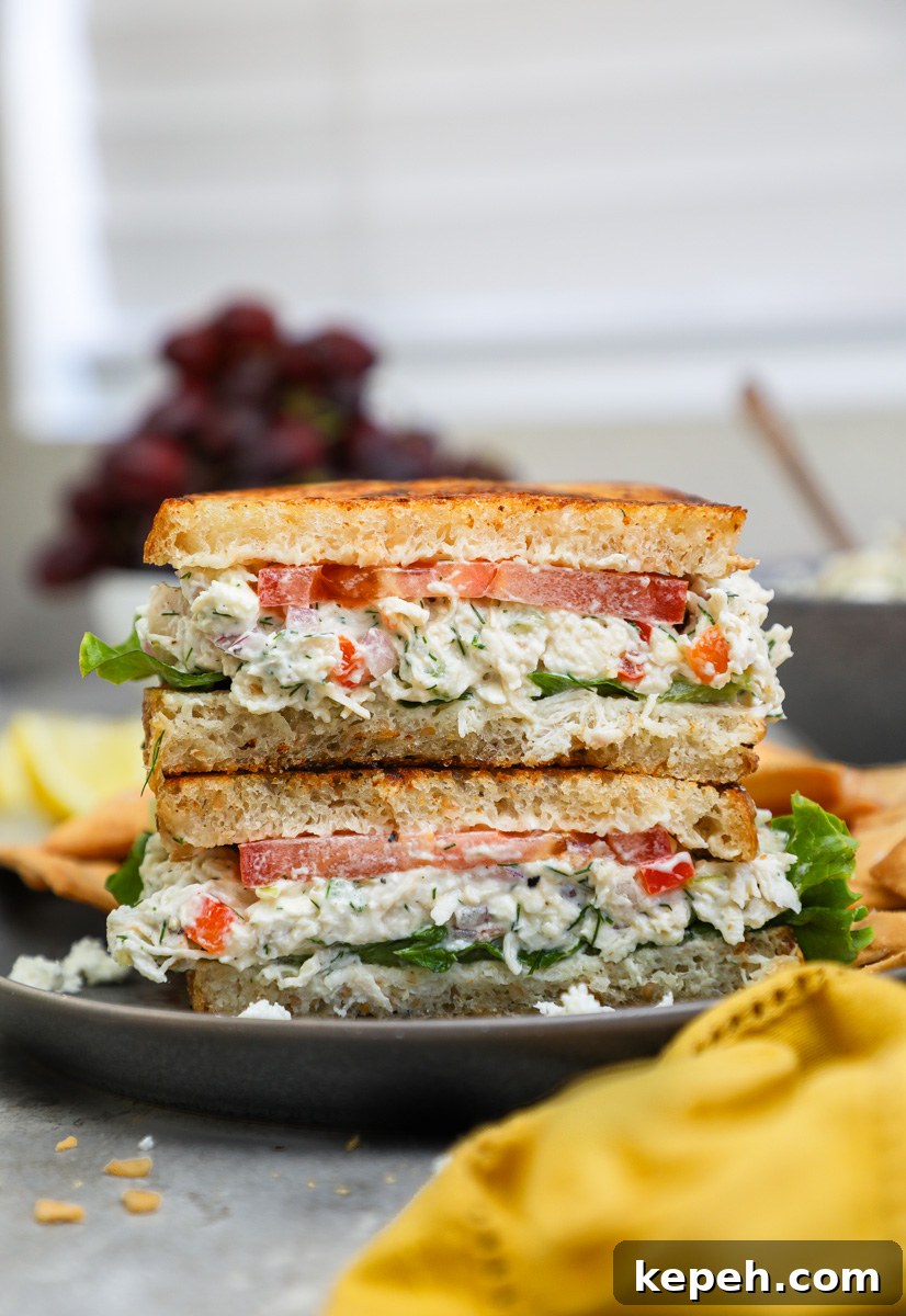 A feta chicken salad sandwich sitting next to a bowl of red grapes and pita chips