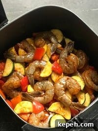 layered Cajun seasoning coated shrimp and veggies in air fryer basket