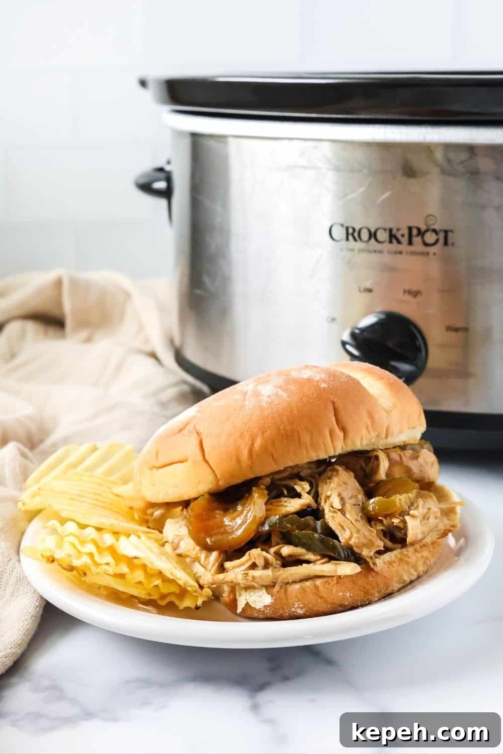 dill pickle chicken sandwich and potato chips on a white plate in front of a Crock Pot.