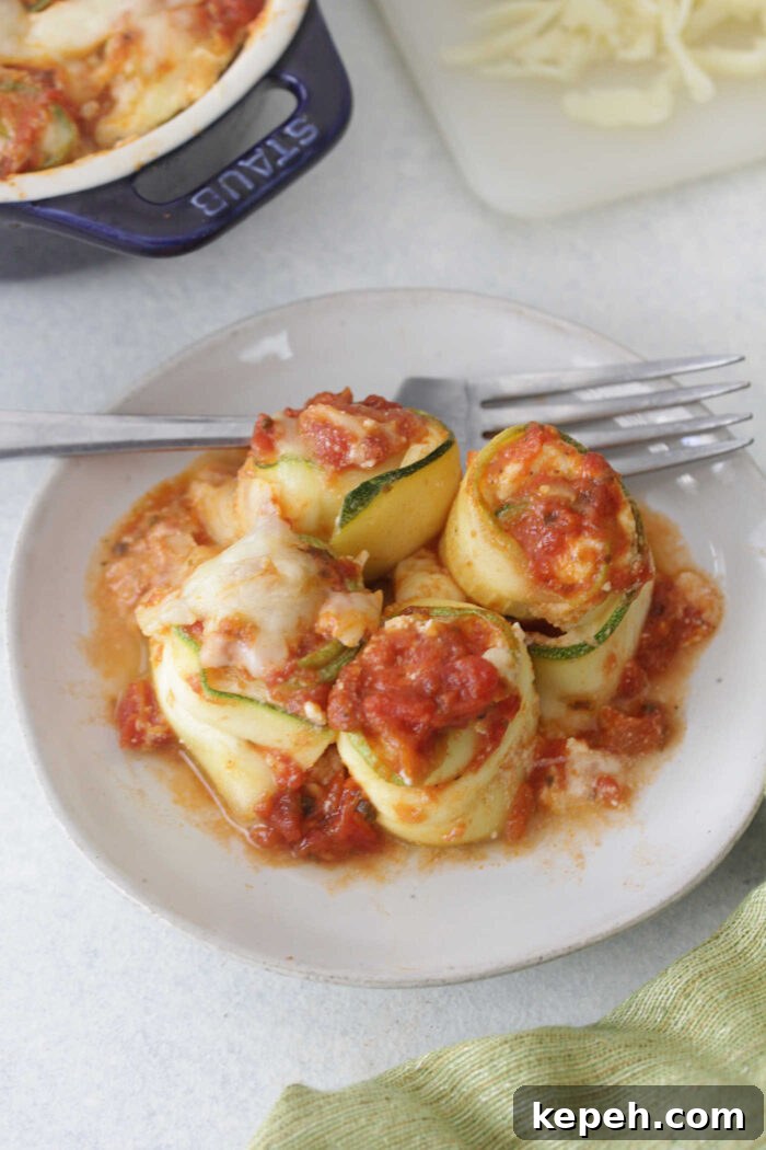 Zucchini Lasagna Roll-Ups with Ricotta & Marinara 5 Close up of baked zucchini lasagna roll ups on a white plate with a fork