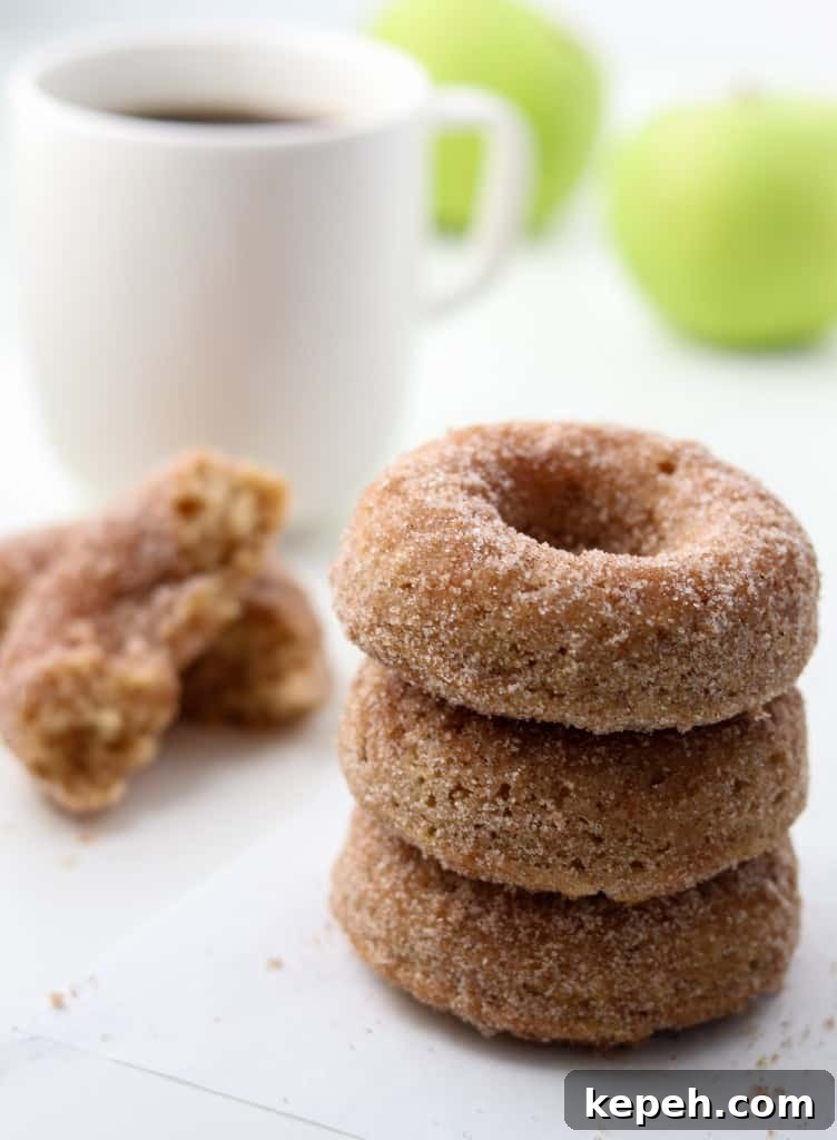 Close up of stack of three apple donuts next to a cup of coffee and apples