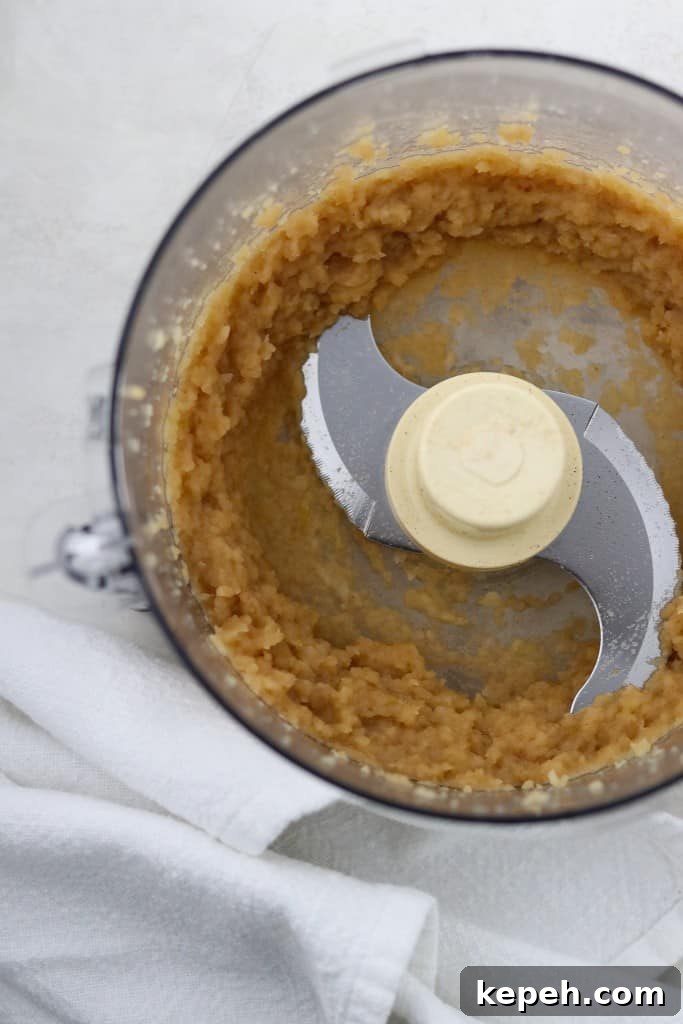 Applesauce in the work bowl of a food processor next to a white towel