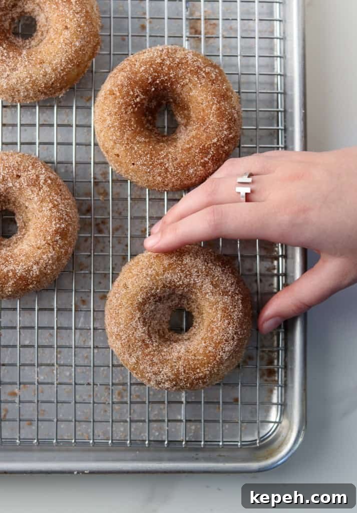 Hand reaching for baked apple donut on a cooling rack
