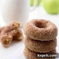 Close up of stack of three apple donuts next to a cup of coffee and apples