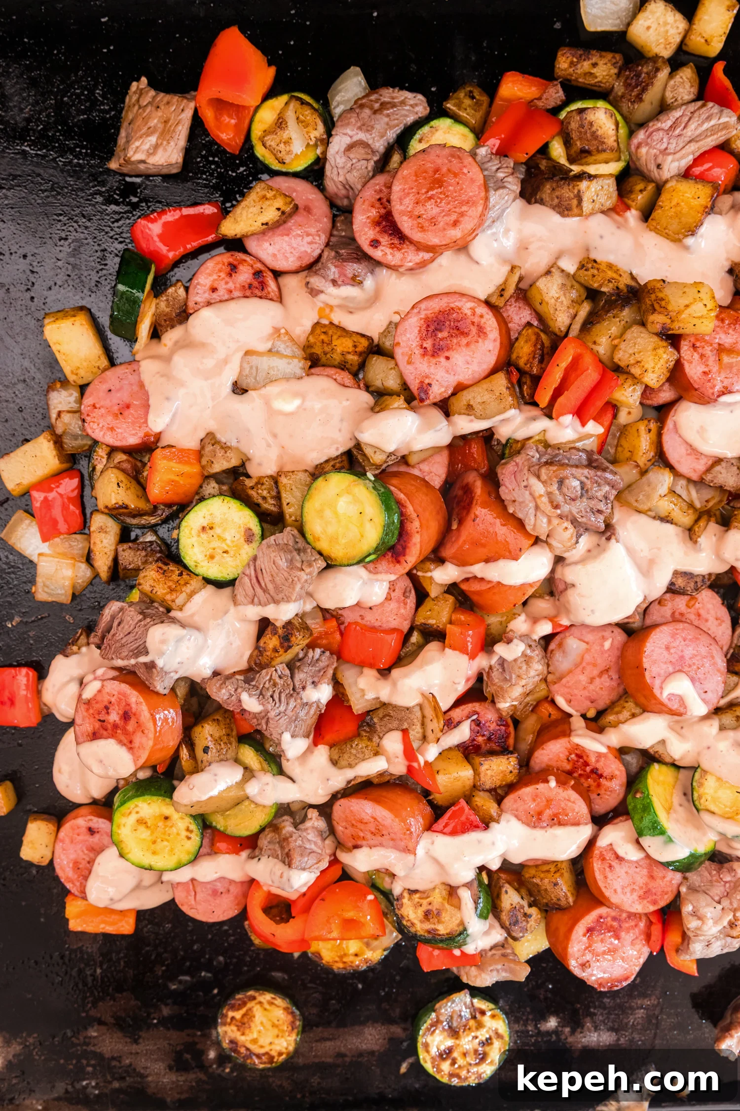 Griddle stir-fry of sausage, beef, potatoes, zucchini, peppers, and onions drizzled with a creamy sauce.