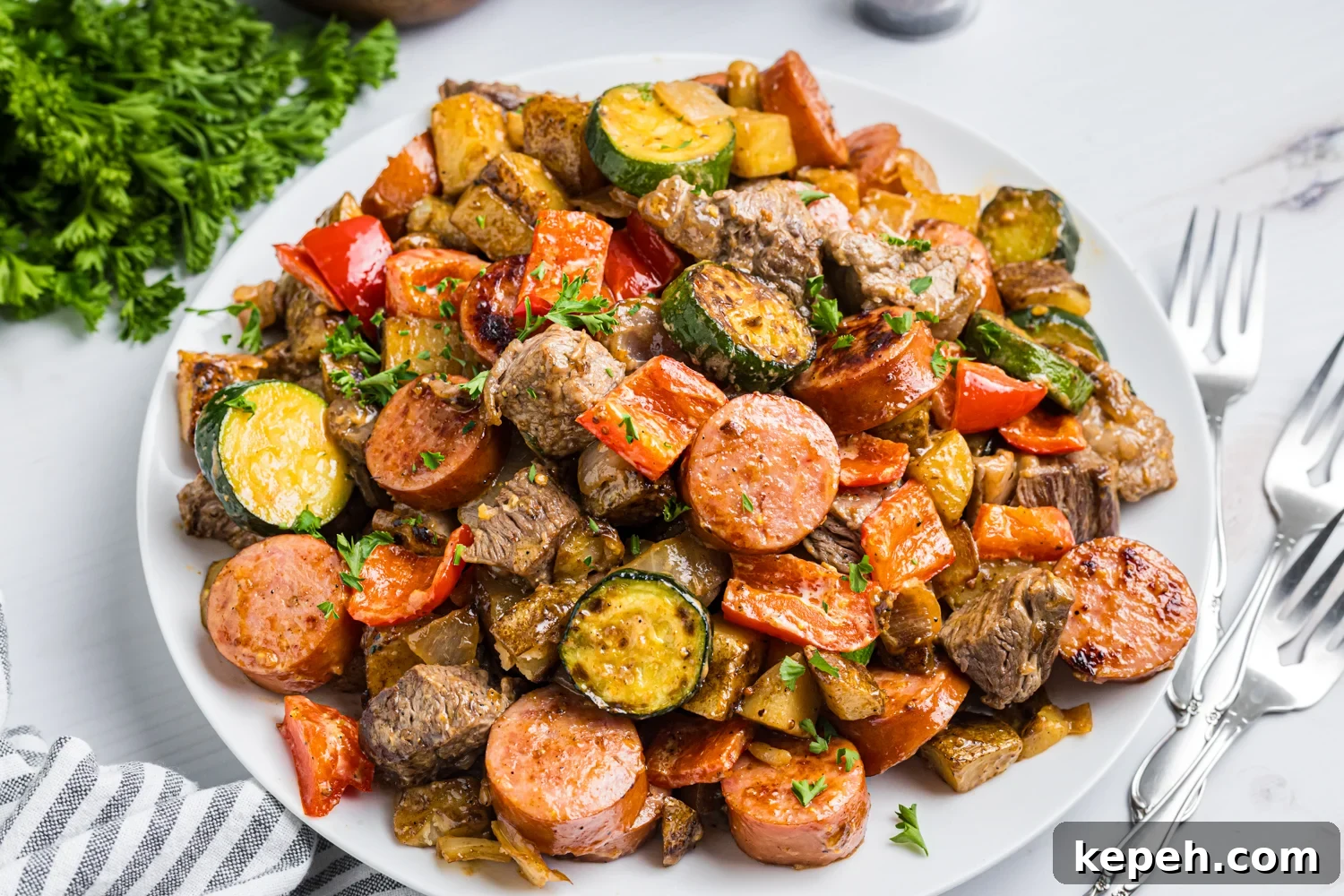 Platter piled with cowboy stir-fry—sausage, beef, potatoes, zucchini, peppers, and onions—sprinkled with parsley, with forks on the side.