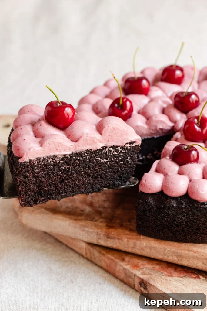 Slice of chocolate olive oil cake topped with cherry ganache and fresh cherries pulling away from the whole cake.