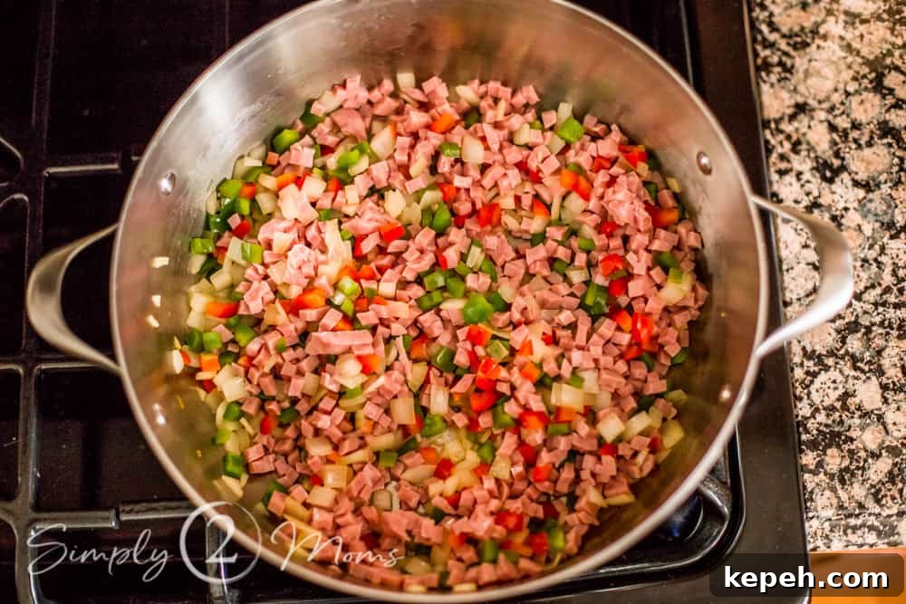 overhead view of chopped onions and peppers and diced ham in a large pan on top of the stove