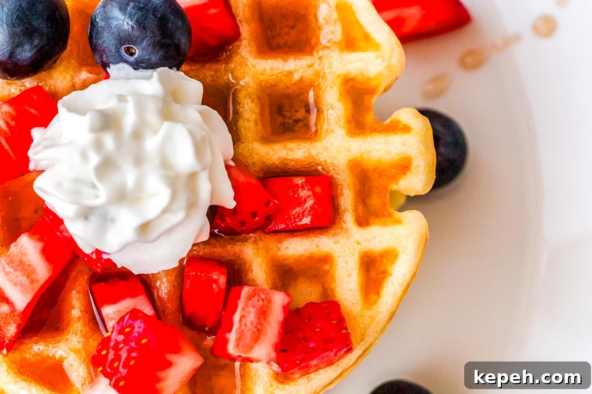 Crispy Dash Waffle Maker Recipes for Quick Breakfasts 3 A waffle on a plate topped with berries, syrup, and whipped cream.