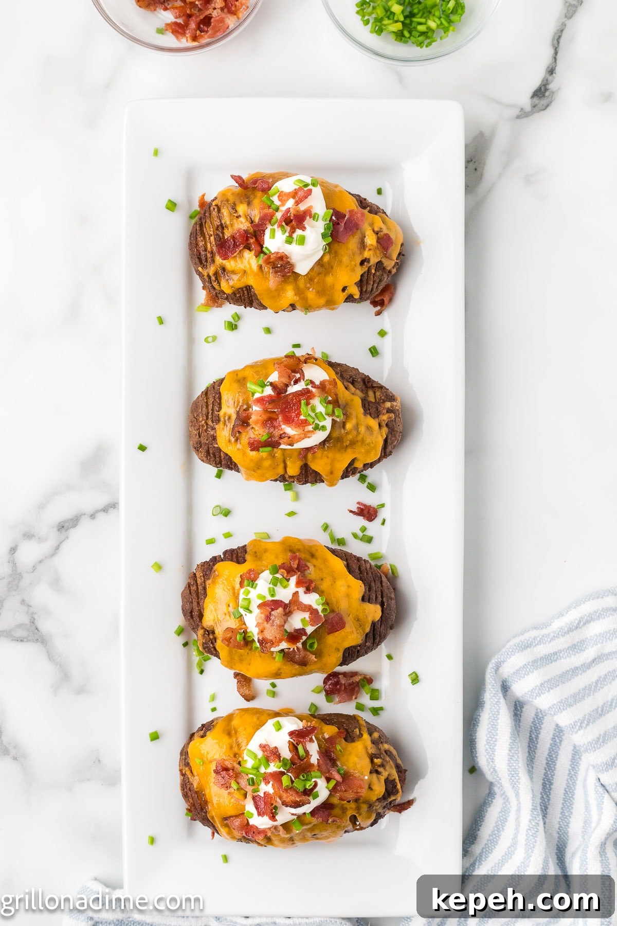 Smoked Hasselback Potatoes with Crispy Herb Butter 8 Smoked Hasselback potatoes on a platter topped with melted cheese, chopped bacon, sour cream and chives