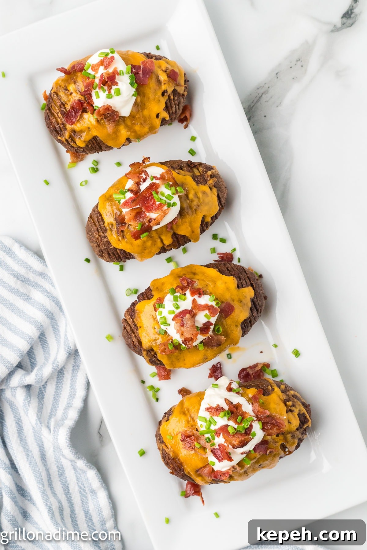 Smoked Hasselback Potatoes with Crispy Herb Butter 9 Smoked Hasselback potatoes on a platter topped with melted cheese, chopped bacon, sour cream and chives