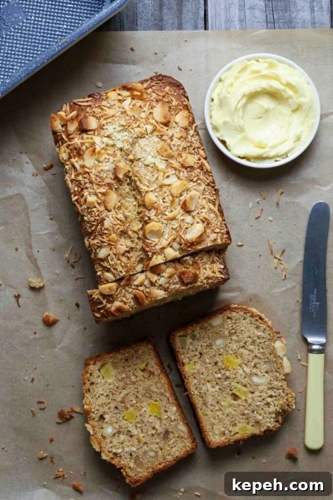 Sourdough Banana Bread with Hawaiian-Style Sweetness 2 Sourdough Hawaiian banana bread on parchment paper with half the loaf sliced next to a knife and small bowl of butter.