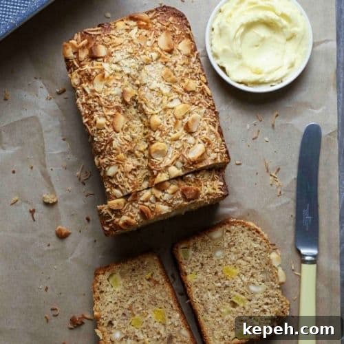Sourdough Hawaiian banana bread on parchment paper with three slices cut next to a small bowl of butter and a butter knife.