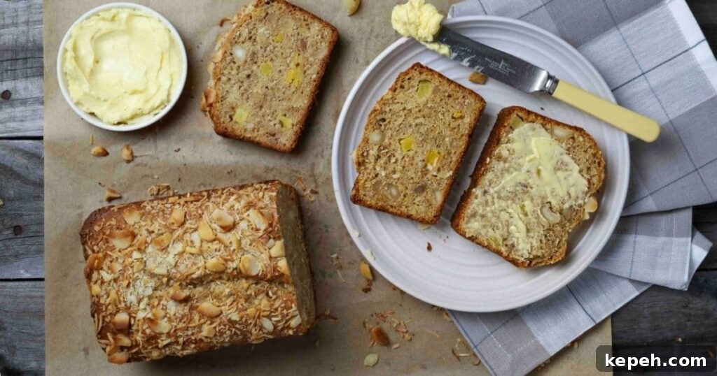 Sourdough Banana Bread with Hawaiian-Style Sweetness 10 Sourdough Hawaiian banana bread on parchment paper with half the loaf sliced and two slices on a white plate with butter.