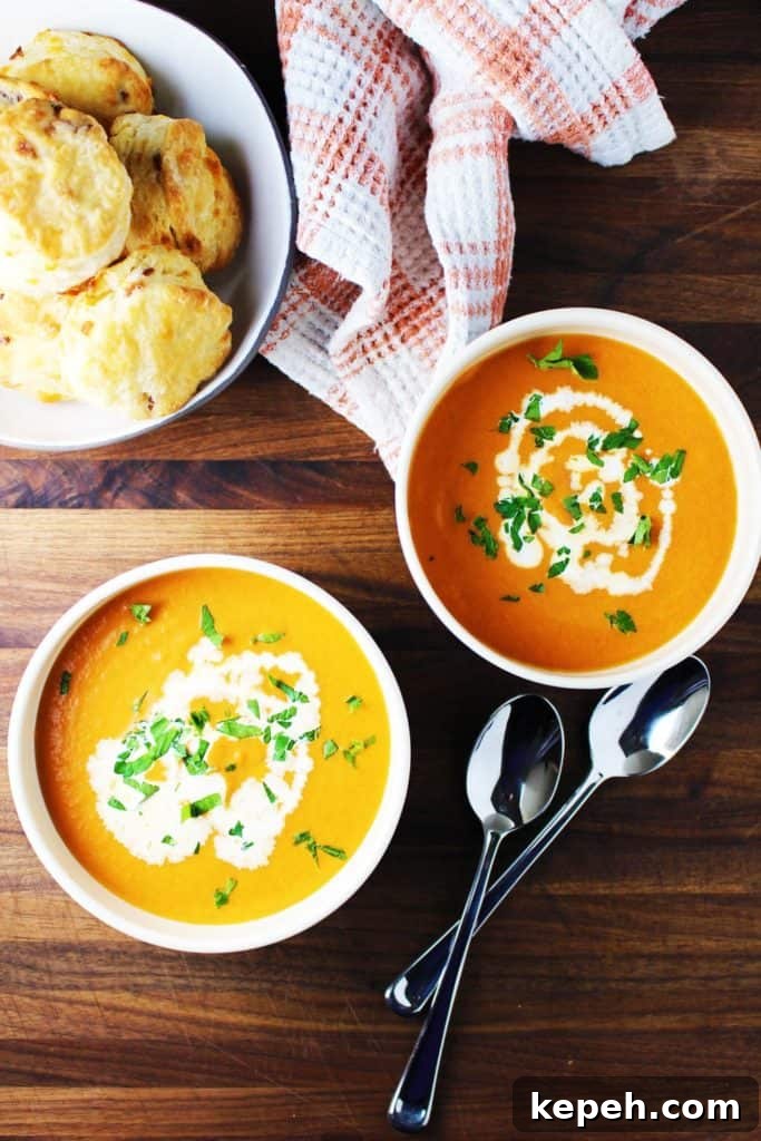 Two bowls of tomato soup garnished with cream and parsley and a bowl of biscuits 