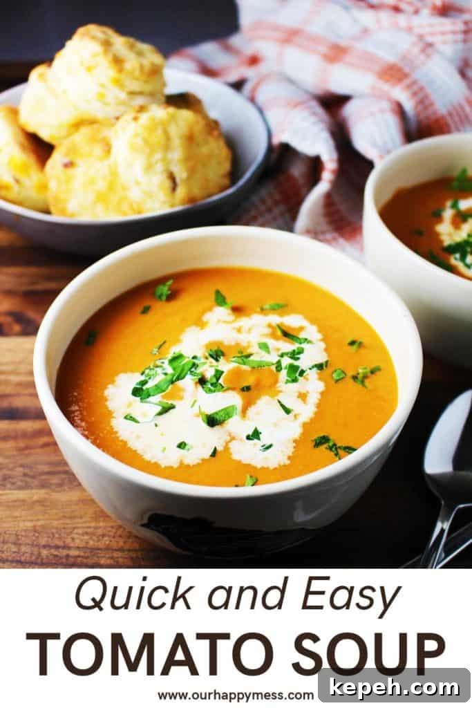 Bowl of tomato soup garnished with cream and parsley, with a bowl of biscuits in the background
