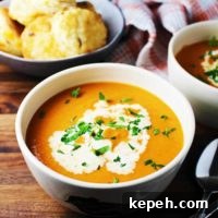 Bowl of tomato soup garnished with cream and parsley, with a bowl of biscuits in the background