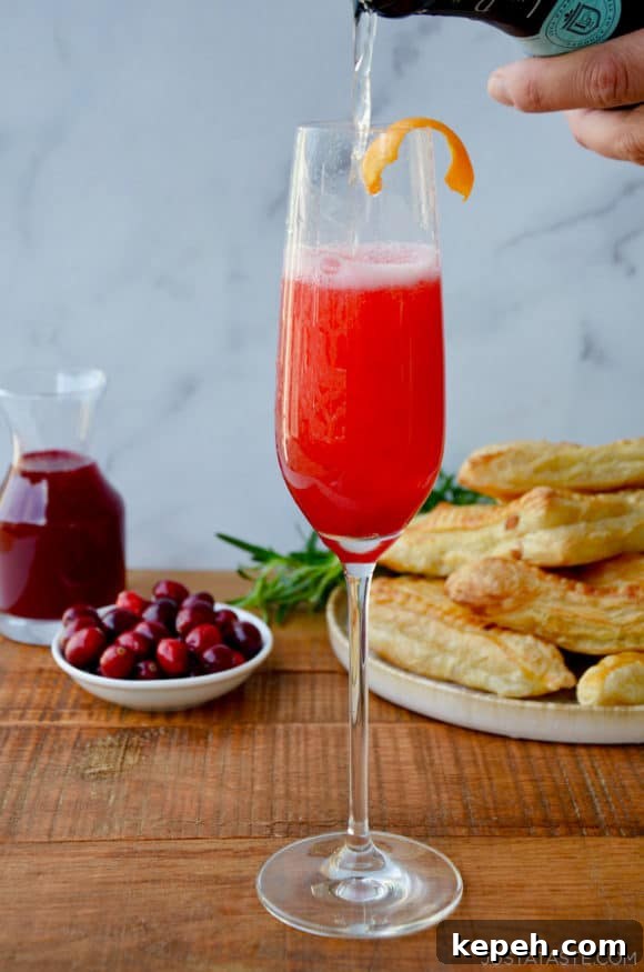 Sparkling Cranberry Champagne Cocktail Recipe for Holidays 4 Cranberry Champagne Cocktail in Champagne flute with orange twist and fresh cranberries and pastries in the background