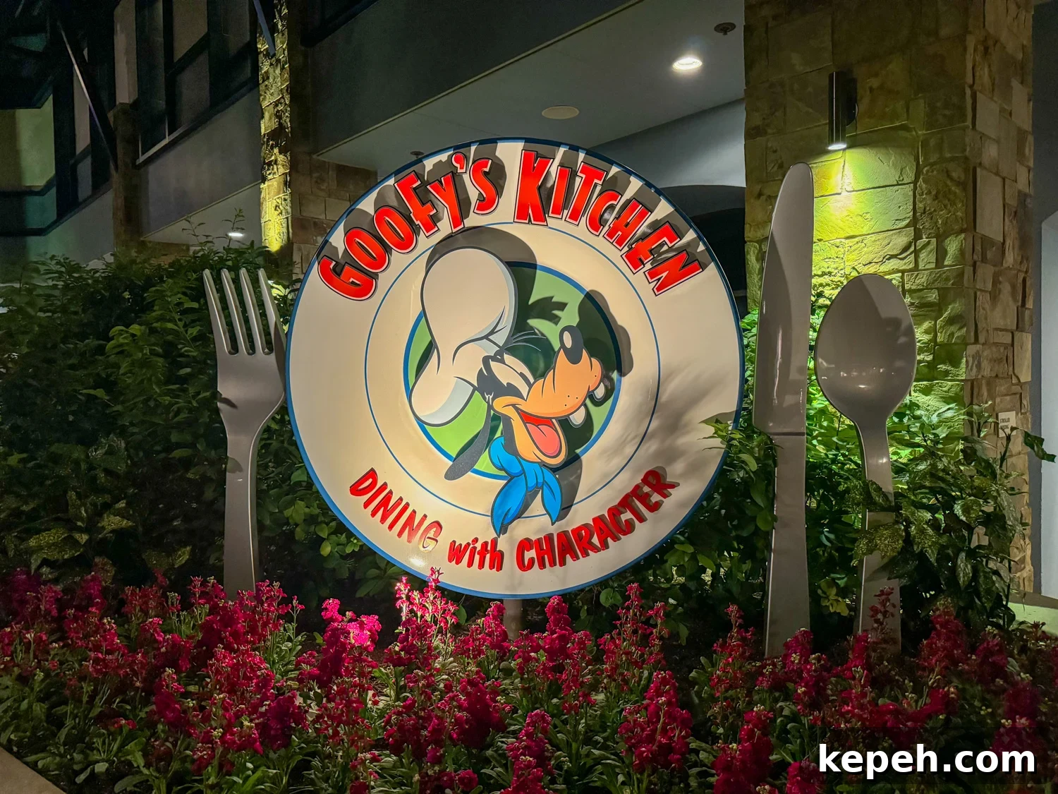 Sign that says Goofy's Kitchen over Goofy's head with a chefs hat and Dining with Character underneath on the plate with a fork, knife and spoon in flowers at the Disneyland Hotel.