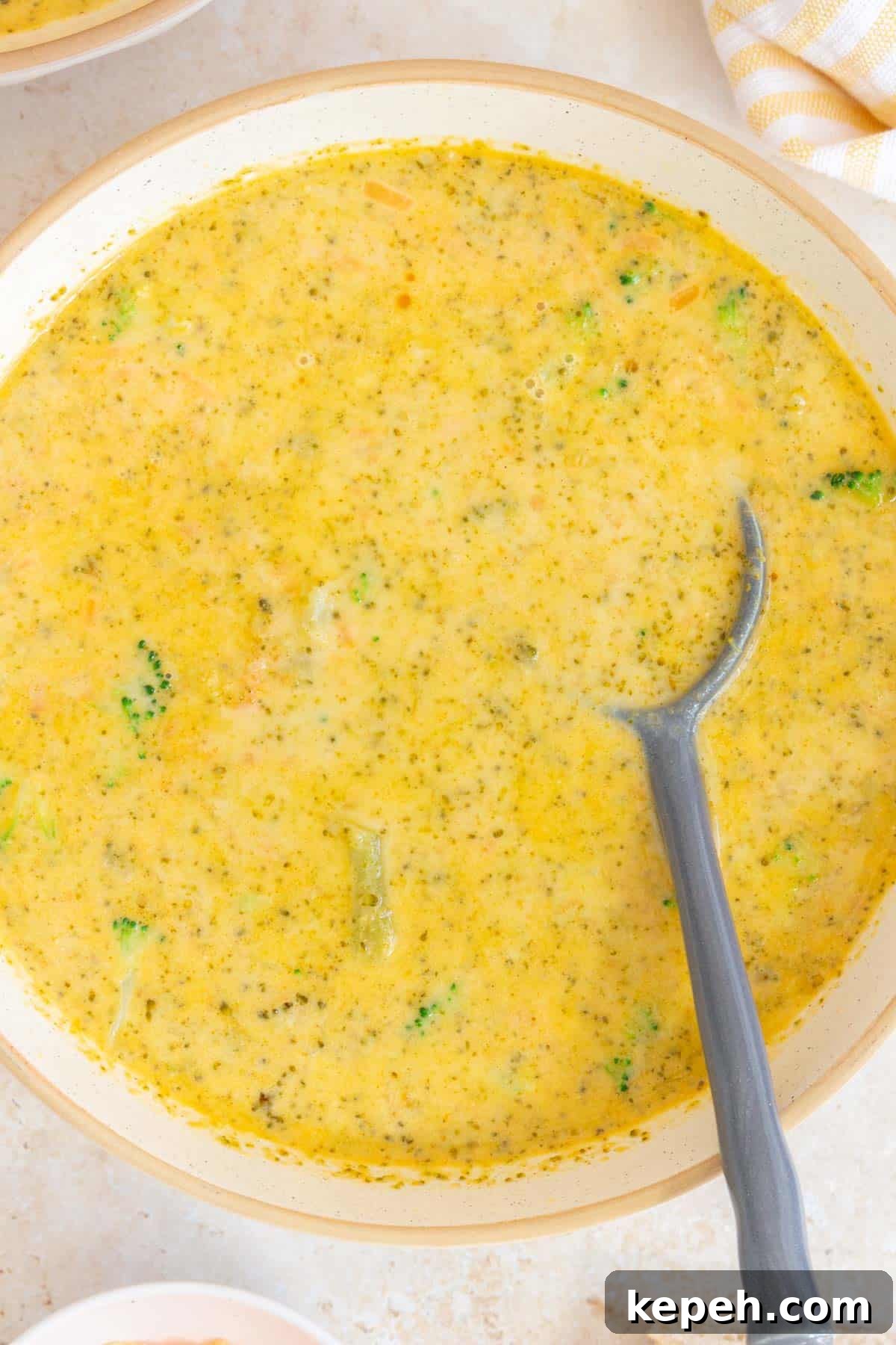 Creamy Instant Pot Broccoli and Cheddar Soup Recipe 7 A close up view of a bowl of Instant Pot broccoli cheddar soup with a grey spoon.