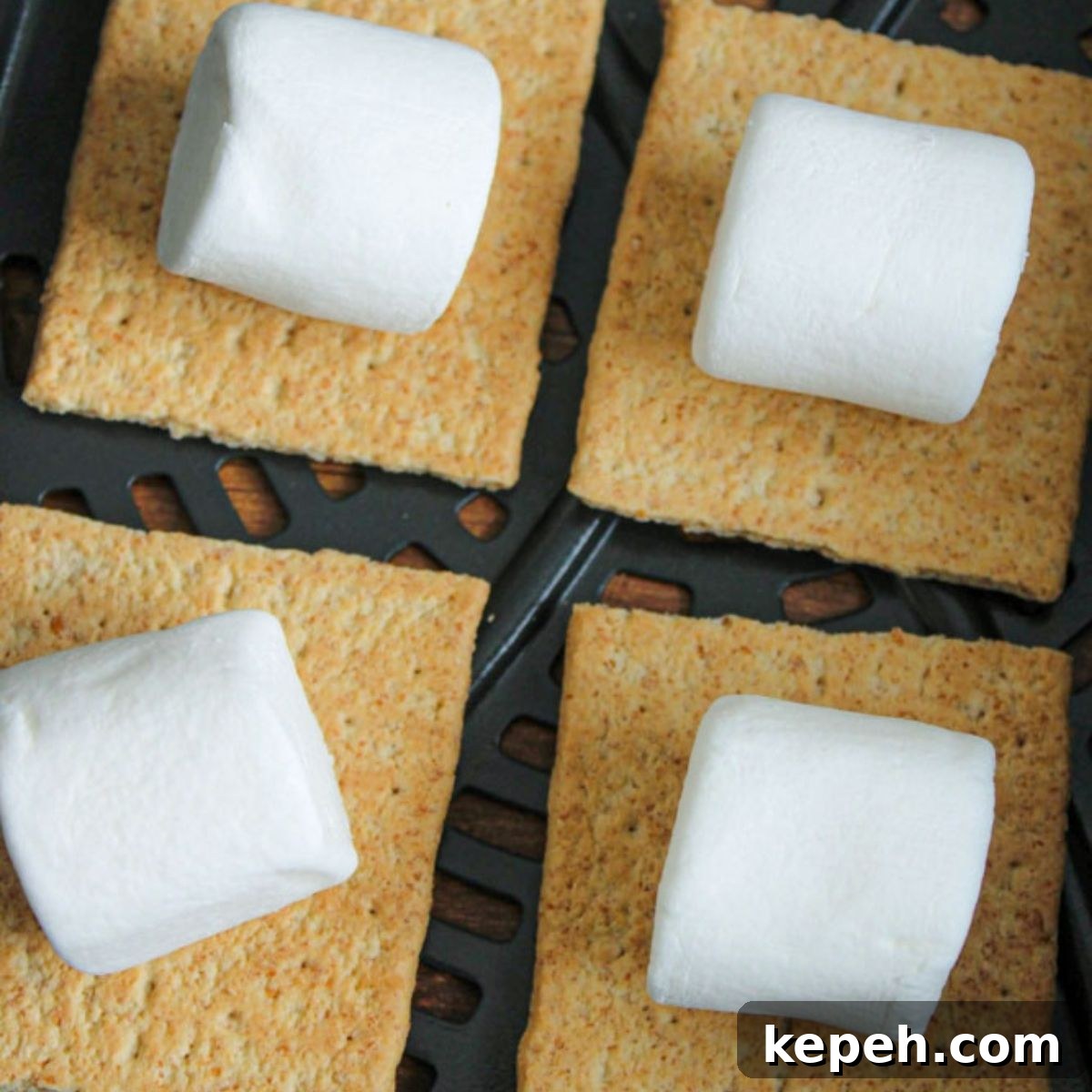 Uncooked marshmallows on graham crackers sitting at the bottom of an air fryer basket.