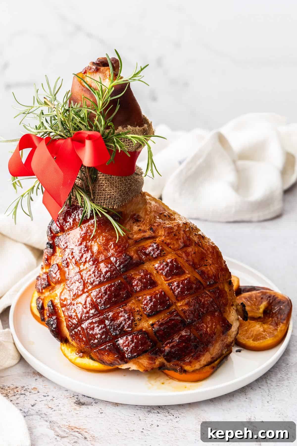 Top Easter Main Courses for a Memorable Holiday Meal 15 Maple Glazed Ham, sitting on some orange slices on a round white plate.