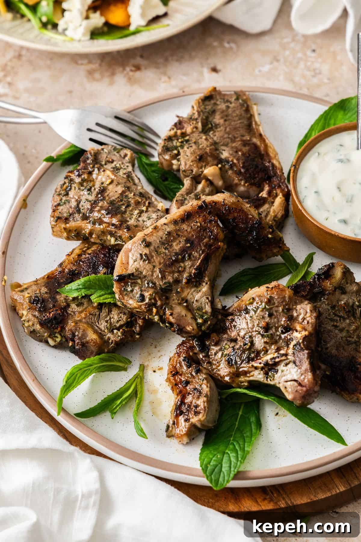 Top Easter Main Courses for a Memorable Holiday Meal 19 Round white plate with cooked Marinated Lamb Loin Chops, with a small bowl of yoghurt sauce on the side, and white cloth.